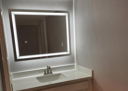 a bathroom vanity with a lighted mirror and sink at The Hillshire Village Apartments